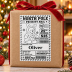 Teddy in Bunny Hood North Pole sticker personalised with Oliver, shown on a wrapped Christmas gift.