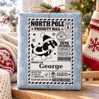 Santa Dog North Pole sticker personalised with George, shown on a wrapped Christmas gift.