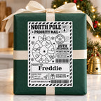 Christmas Wreath North Pole sticker personalised with Freddie, shown on a wrapped Christmas gift.